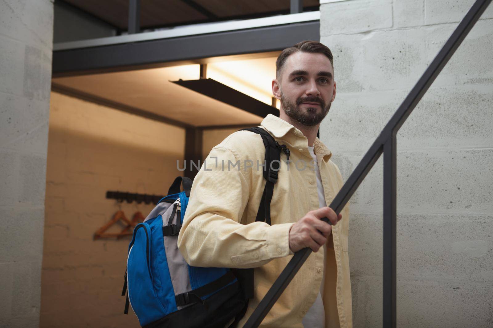 Handsome bearded male tourist with a backpack walking up the stairs at his hotel room