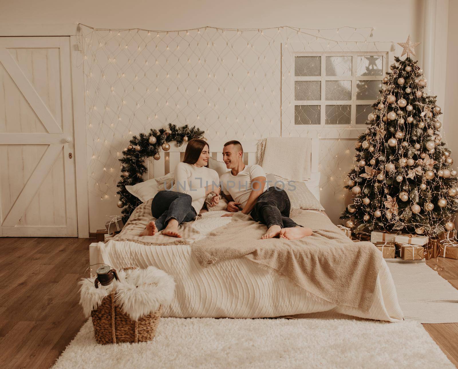 couple man and woman lie on bed bedroom near christmas tree.decorated house for New Year.Christmas morning. apartment interior. Valentine's Day celebration