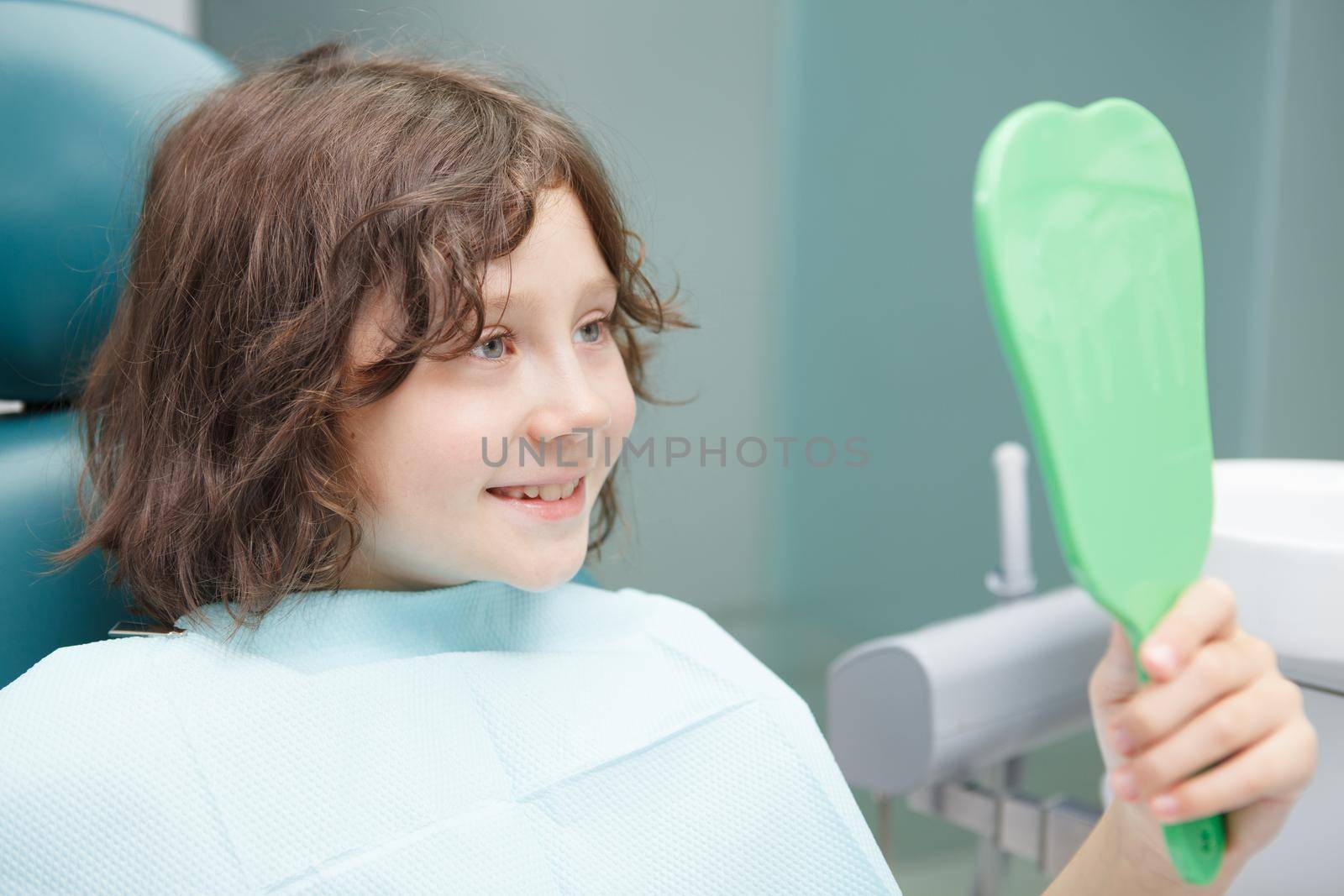 Close up of a cute happy boy examining his teeth in the mirror after dental treatment