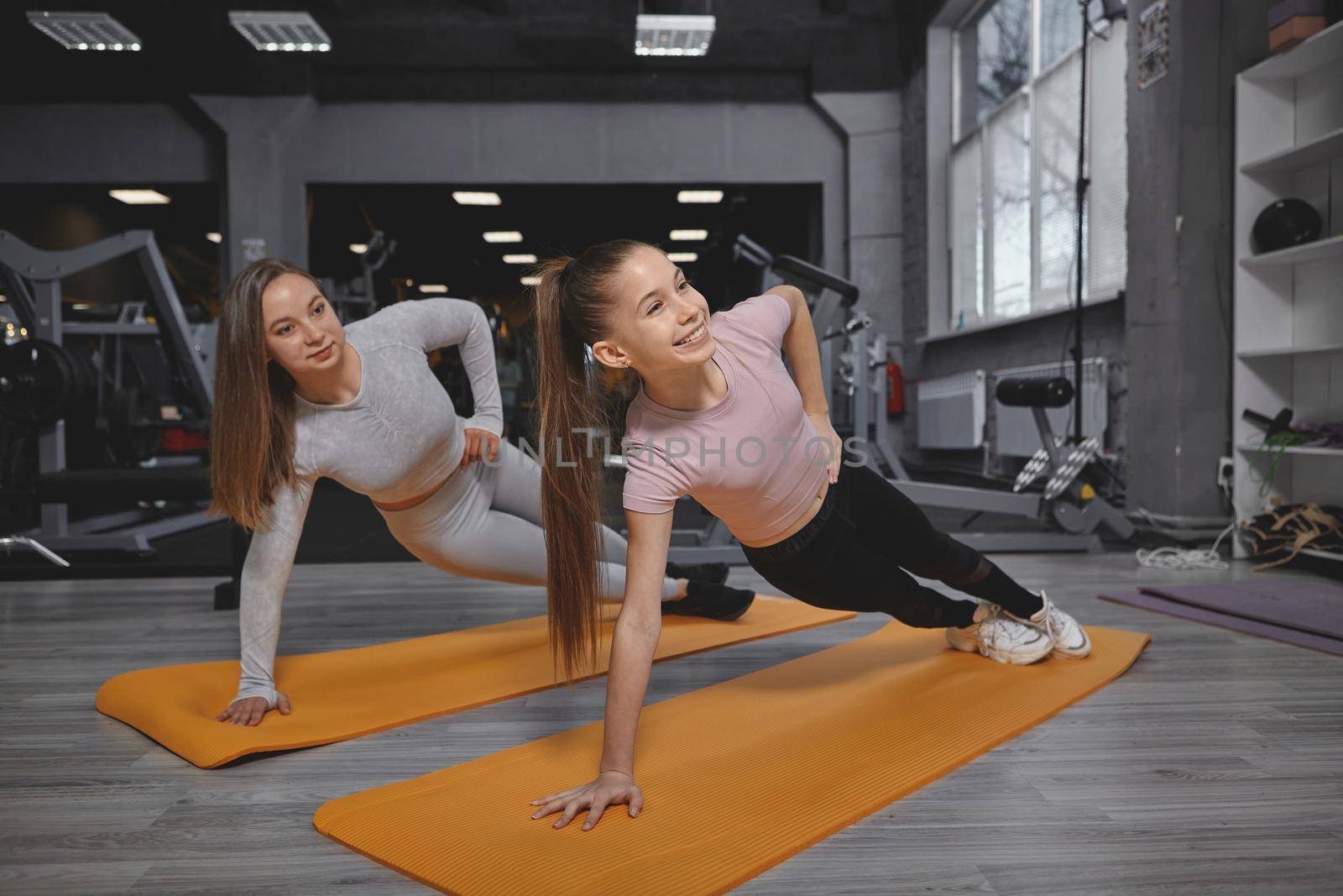 Teenage girl doing plank exercise at the gym, working out with personal trainer