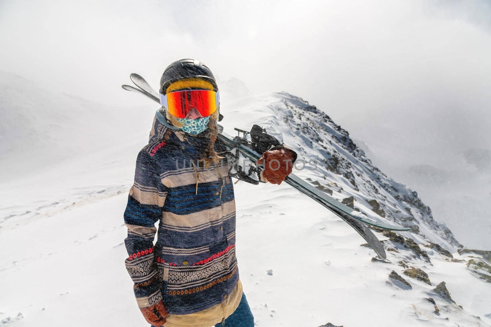 Portrait of a pretty and active woman skier, wearing a mask and holding skis in her hands, active winter holidays. extreme lifestyle concept