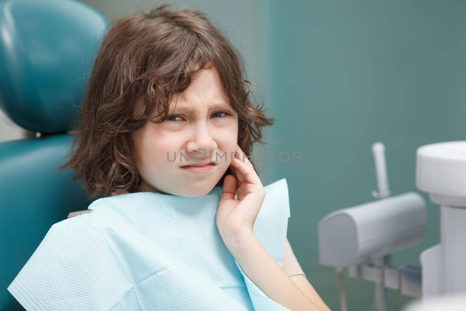 Close up of a little boy having toothache, sitting at dentists office