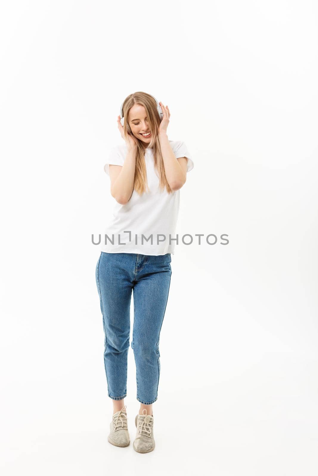Lifestyle Concept: Portrait of a cheerful happy girl student listening to music with headphones while dancing isolated over white background by Benzoix