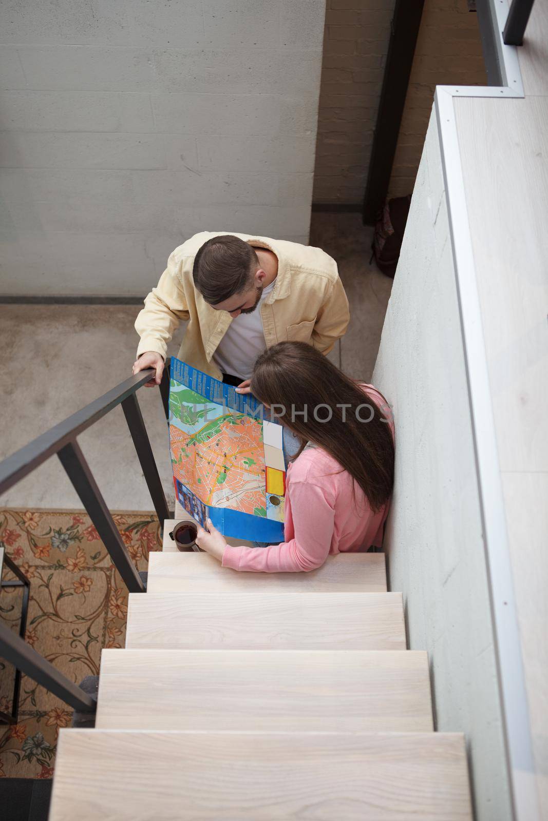 Vertical top view shot of a couple examining city map at their hotel room, sitting on the stairs