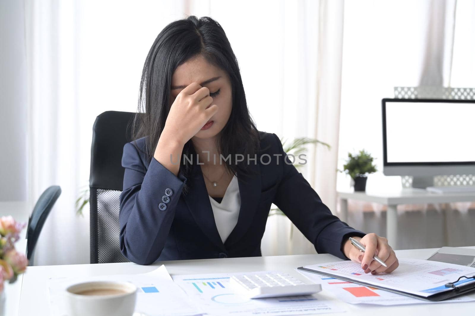 Stressed businesswoman looking worried, tired and overwhelmed while working at office desk.