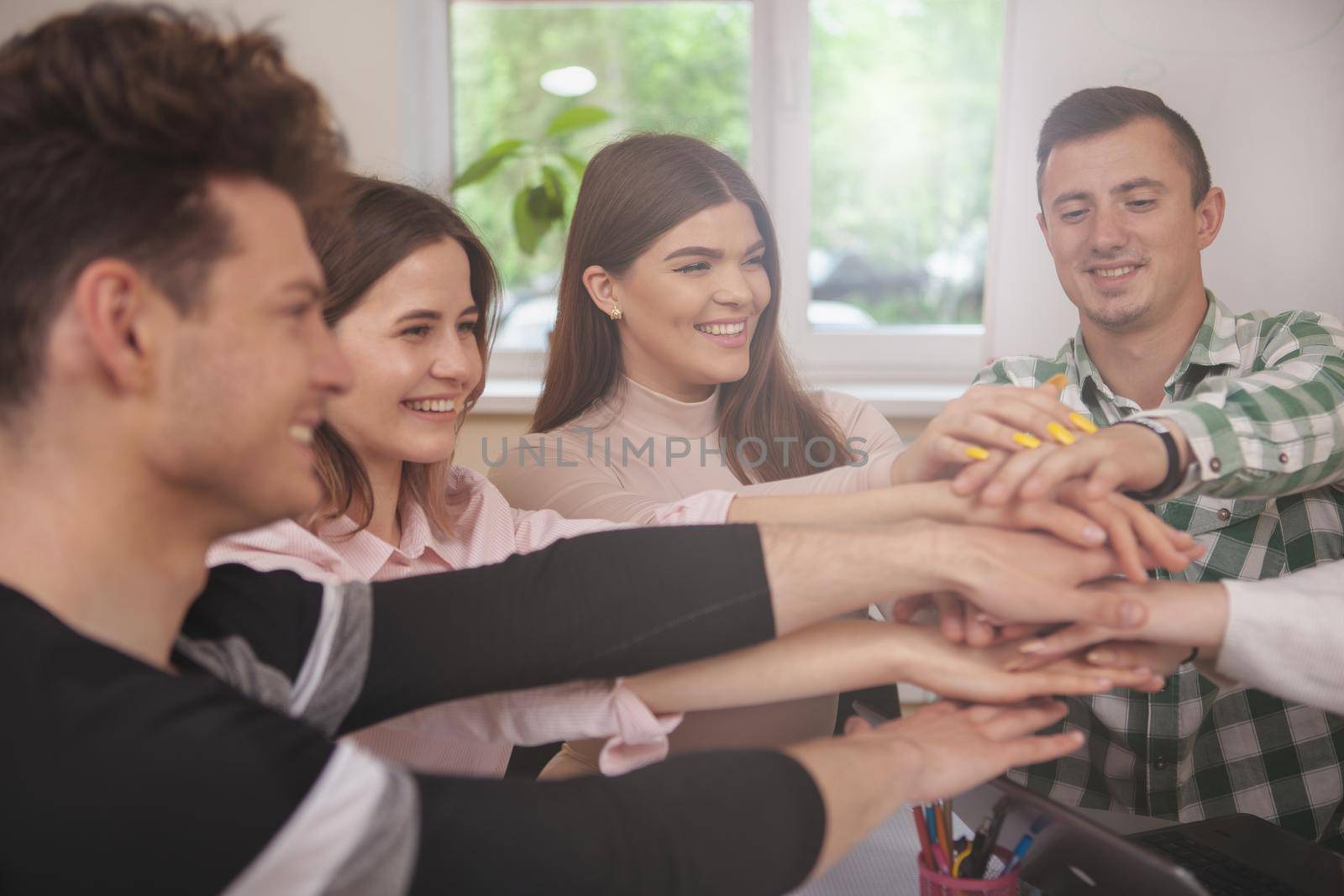 Unity, achievement, joining concept. Cropped shot of a group of college students laughing, putting their hands together. Cheerful young peoople with stack of hands showing teamwork and support