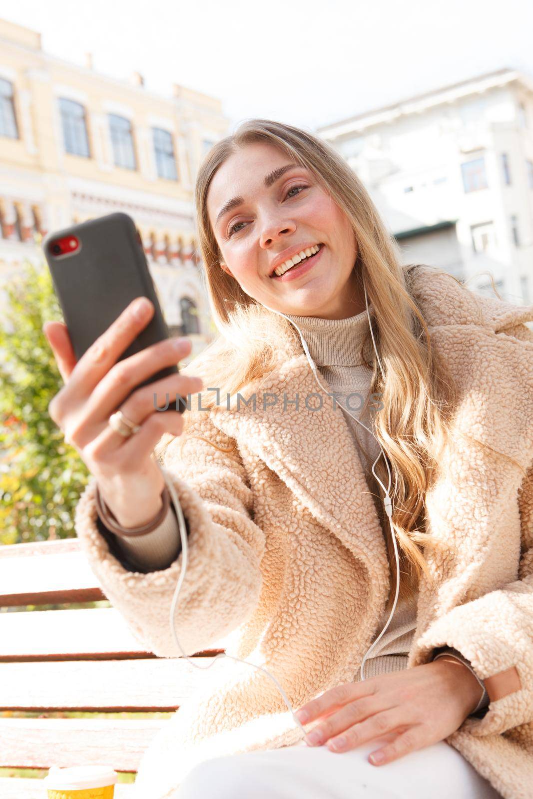 Vertical shot of a cheerful woman listening to music on her smart phone, wearing earphones