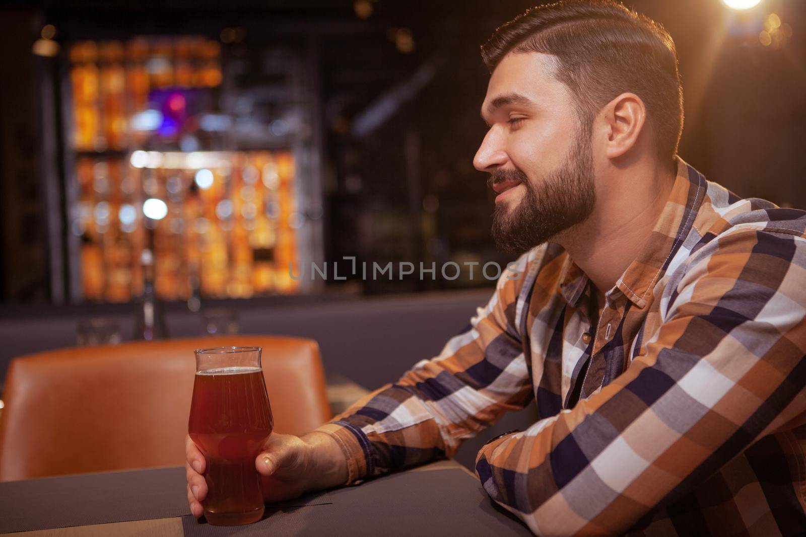 Profile shot of a handsome bearded man smiling joyfully, drinking delicious craft beer at the pub, copy space