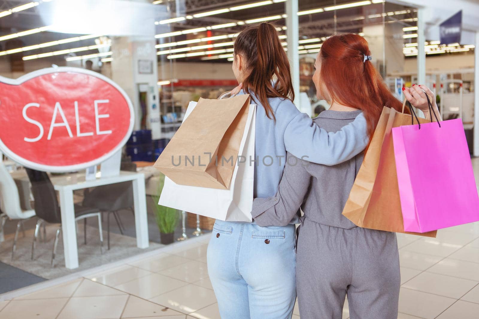 Rear view shot of two women enjoying shopping together, carrying shopping bags, looking at the display of a store