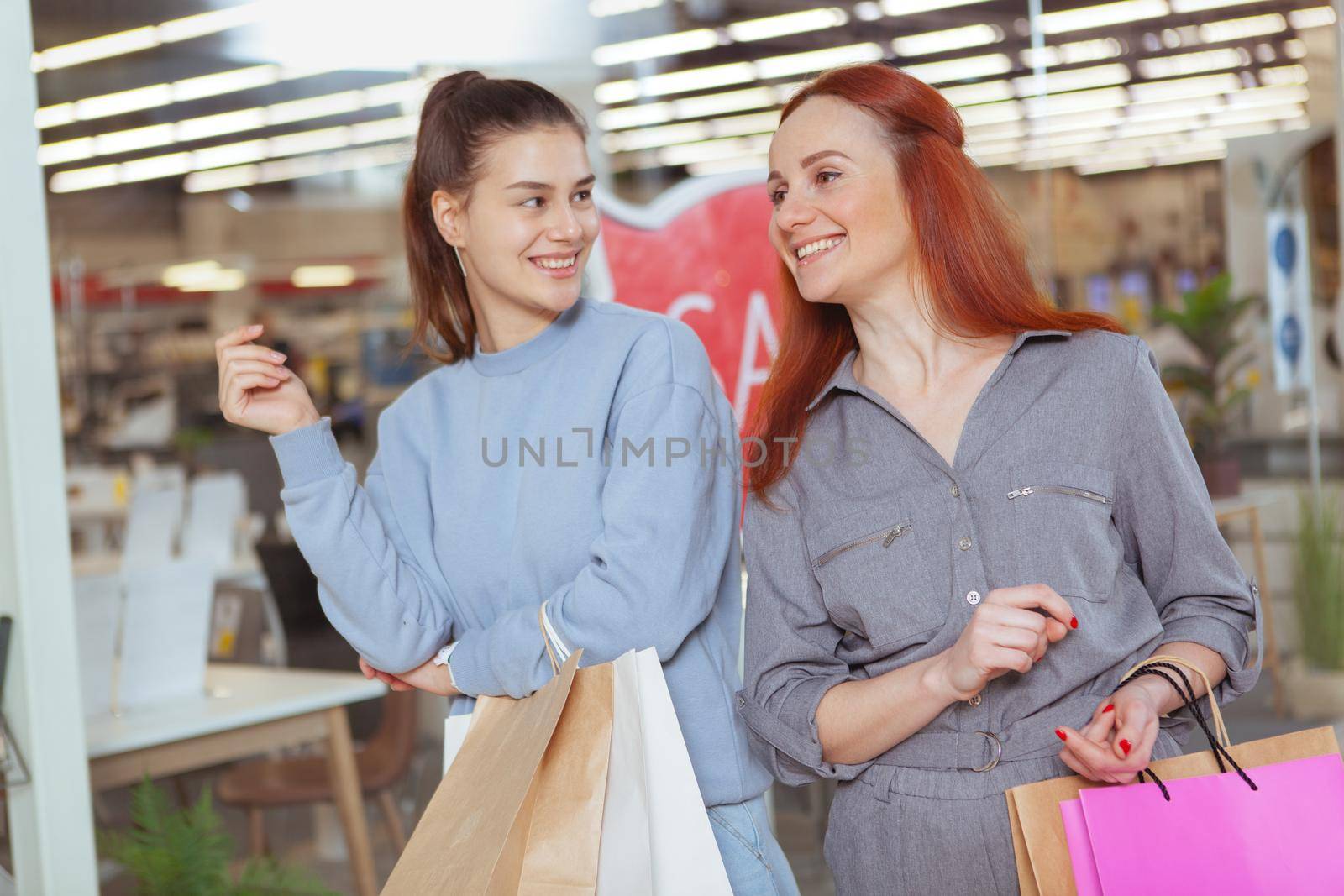 Happy female friends laughing, enjoying shopping together at the mall