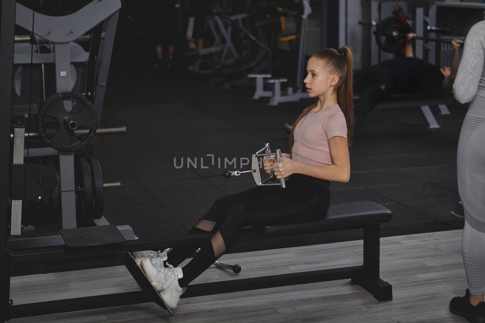 Teenage girl exercising on rowing gym machine, copy space