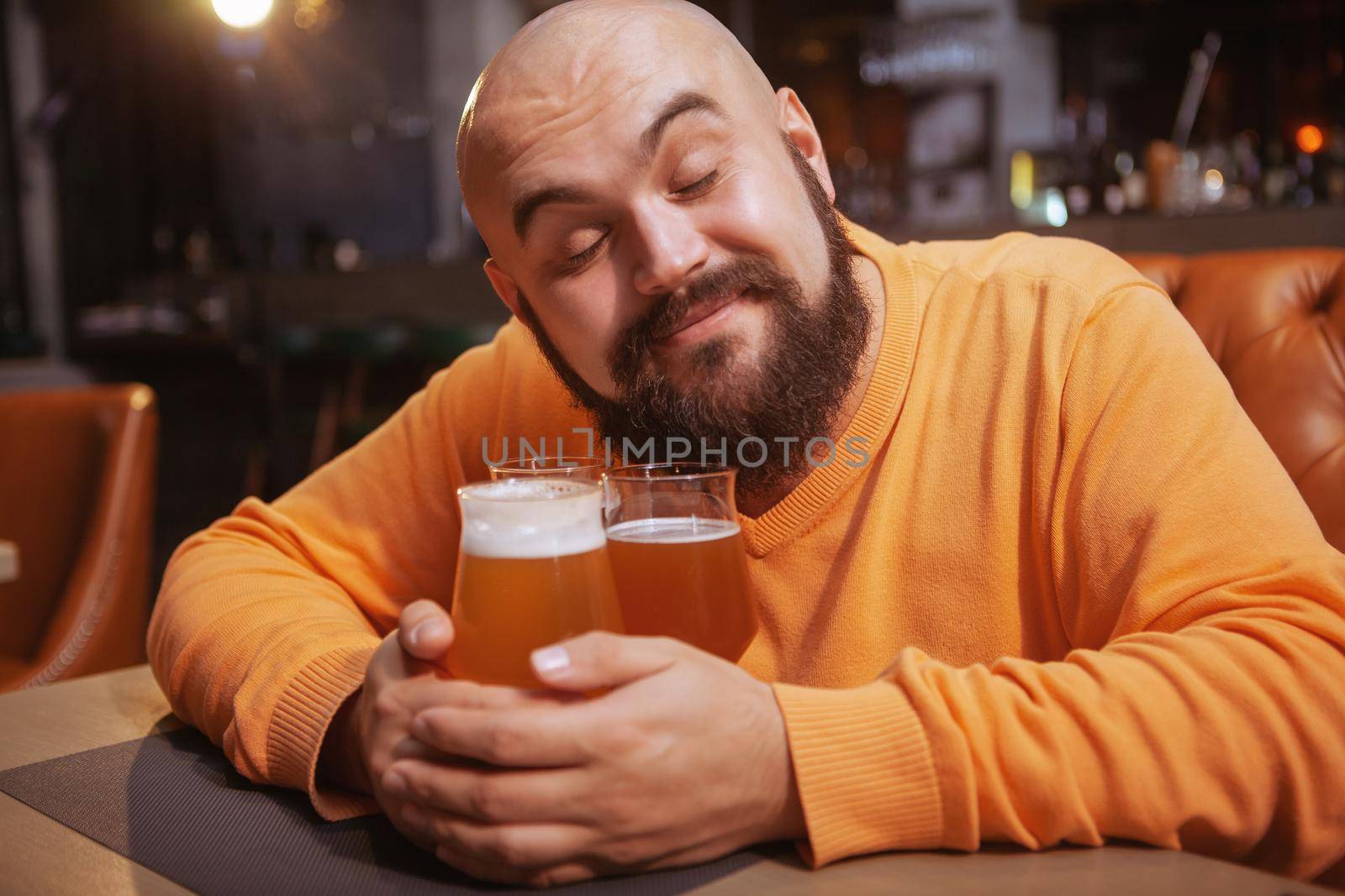 Charming young man smiling with his eyec closed embracing beer mugs. Happy man hugging beer glasses