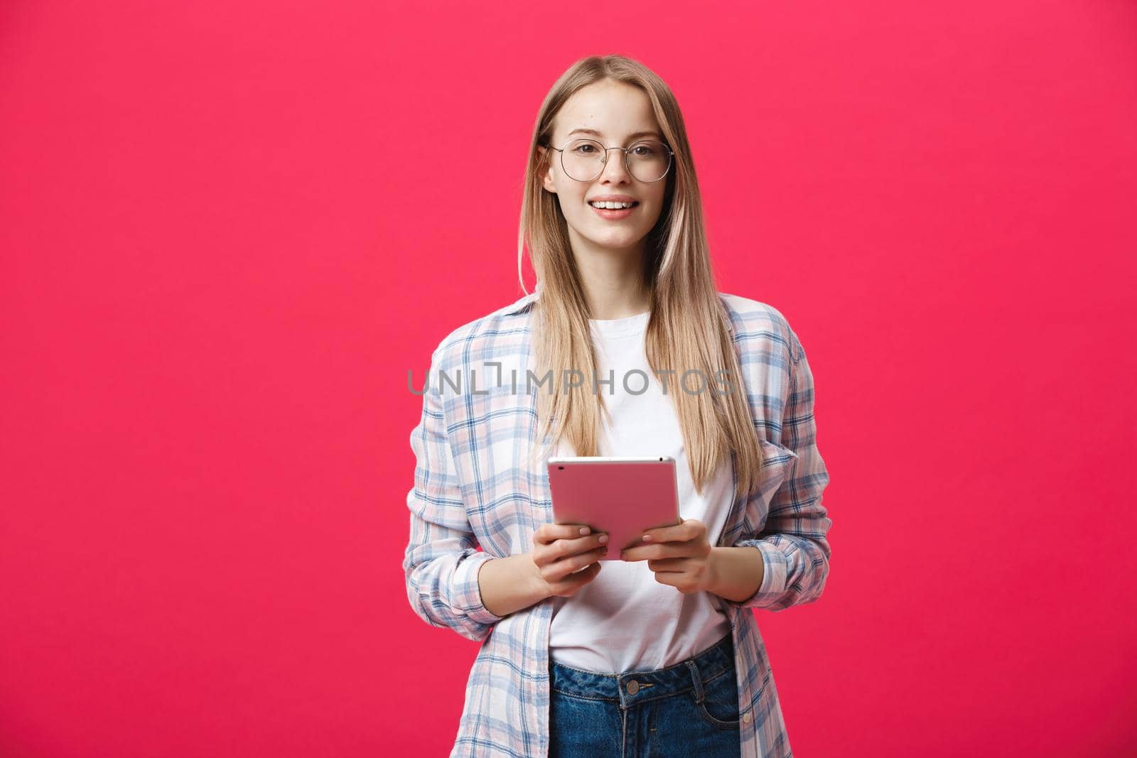 Portrait of a laughing woman using tablet computer isolated on a pink background and looking at camera.