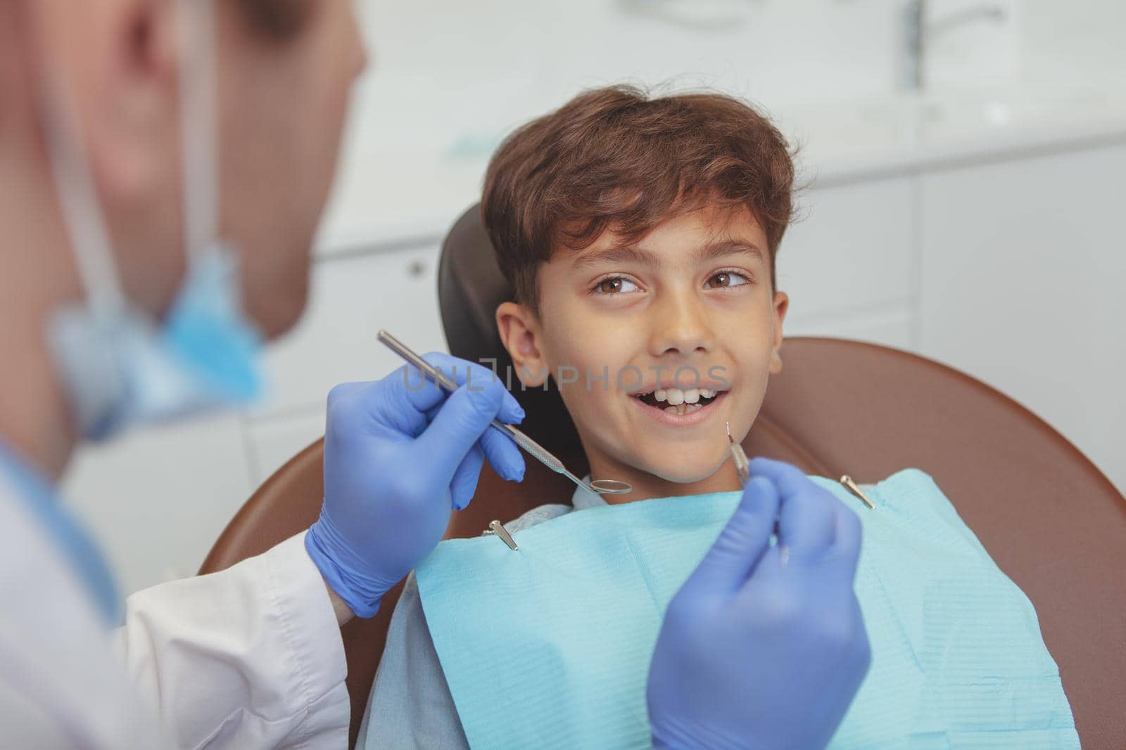 Adorable young boy visiting dentist, having his teeth checked by dentist. Lovely happy kid smiling with healthy teeth, getting his dental examination