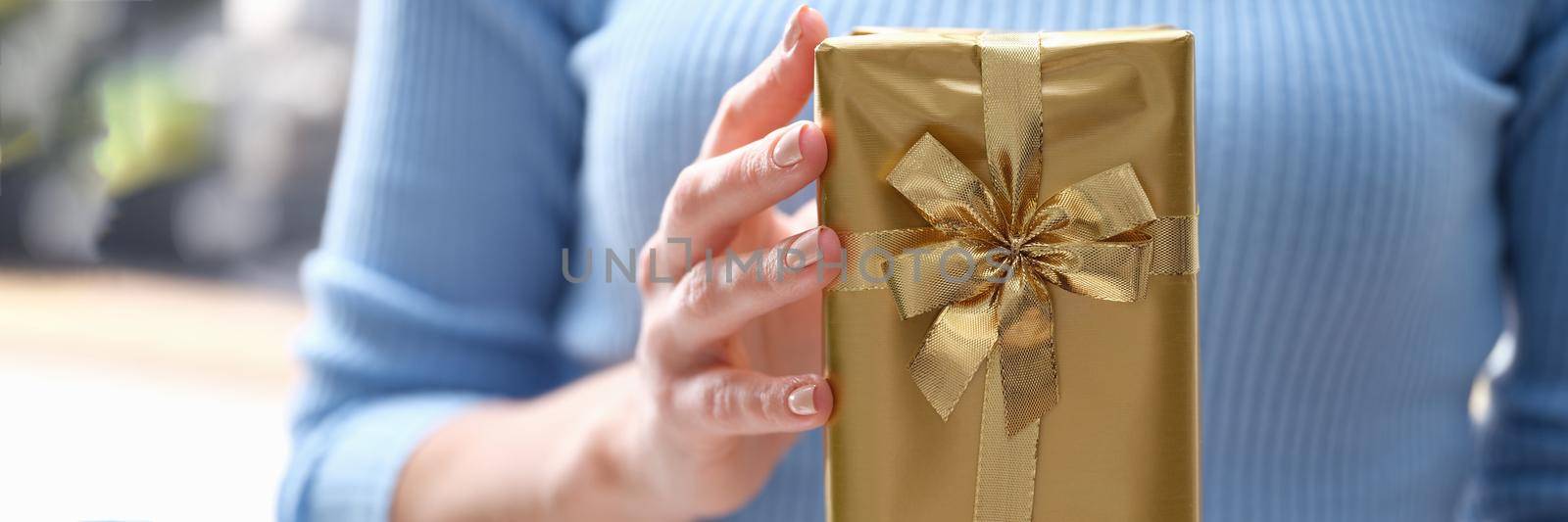 A woman is holding a gift in a gold package with a ribbon, close-up. A beautiful gift for a holiday, vintage giftbox