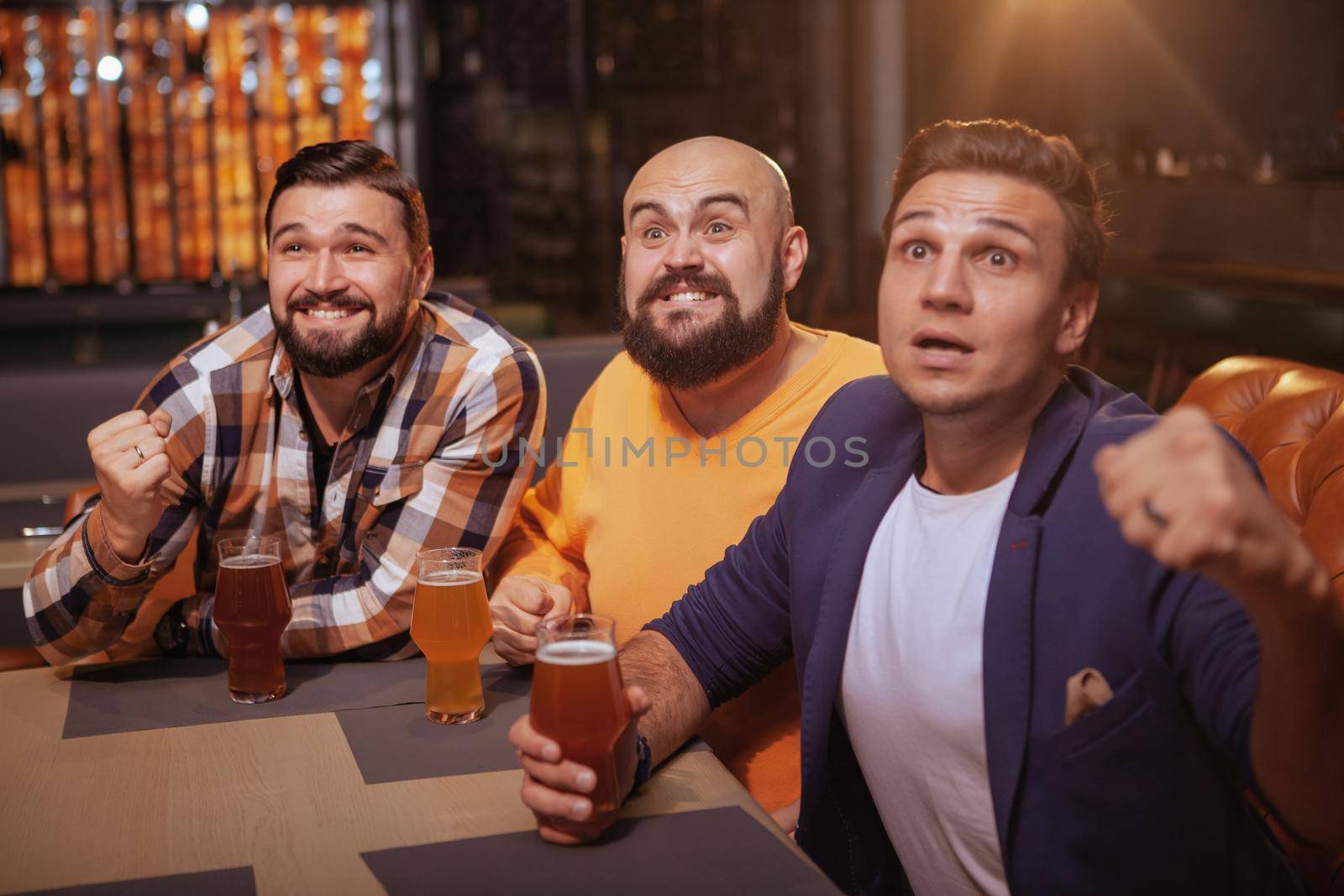 Group of male soccer fans watching a game at sports bar, drinking beer. Men screaming while watching football match at beer pub