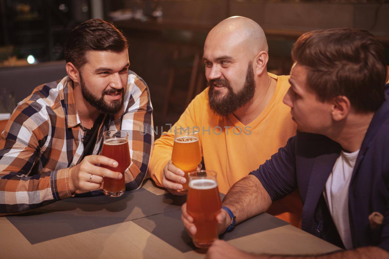 Male friends talking at the bar. Group of men chatting while drinking beer together