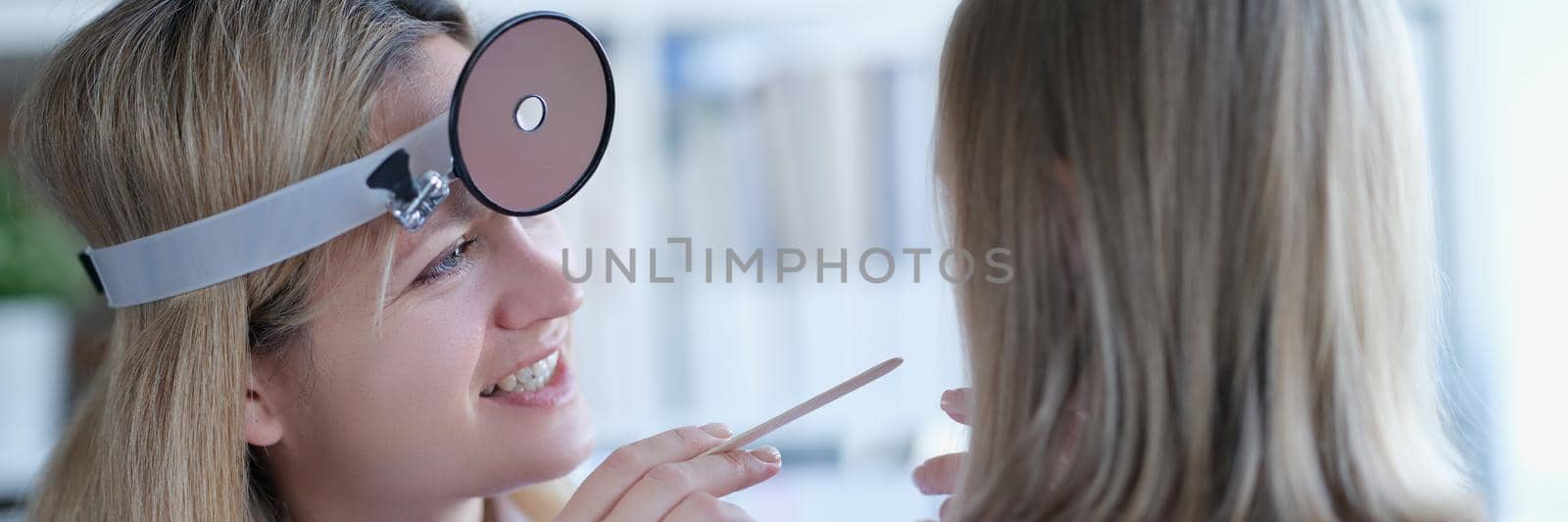 Children's doctor looks at the throat of a little girl by kuprevich