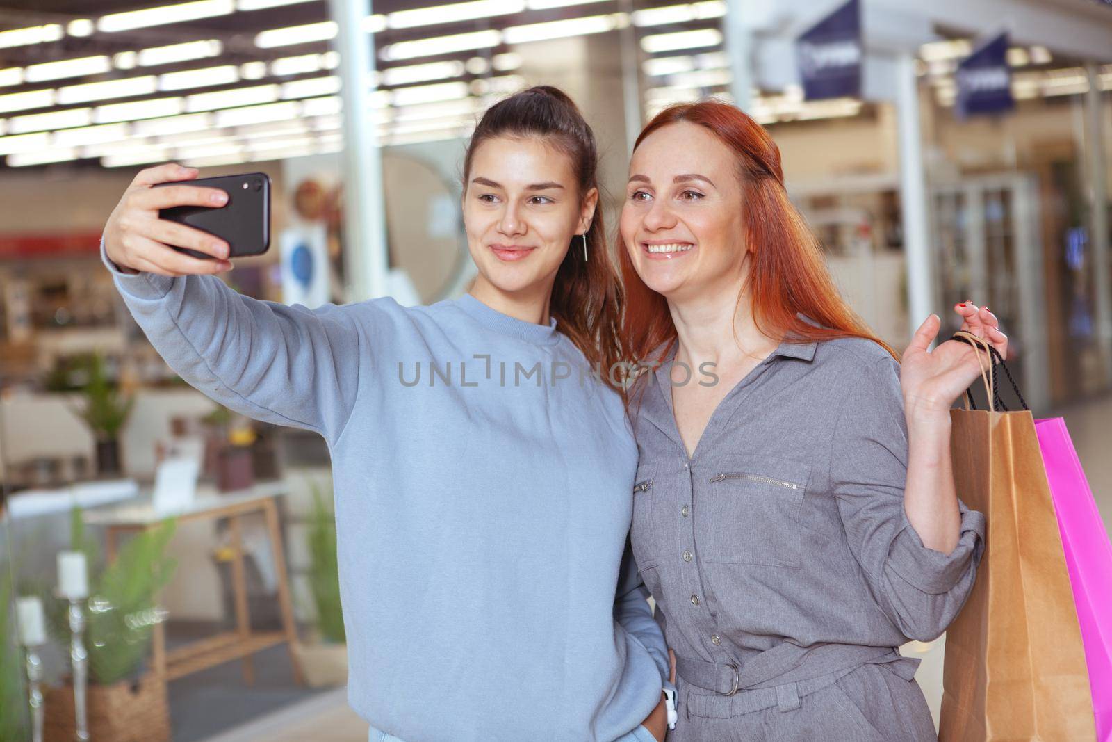 Young beautiful woman taking selfie with her friend while shopping at the mall together