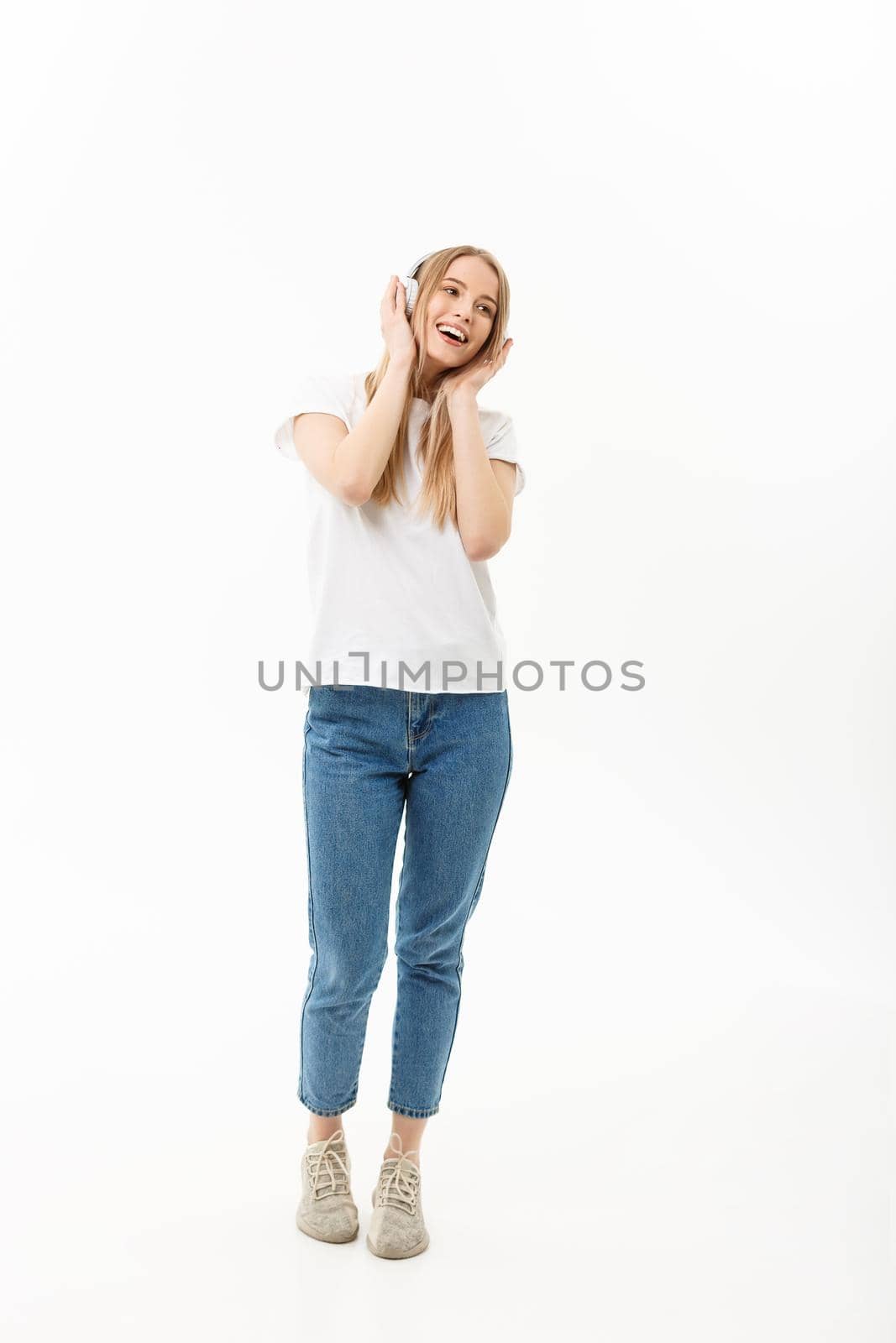 Lifestyle Concept: Portrait of a cheerful happy girl student listening to music with headphones while dancing isolated over white background.