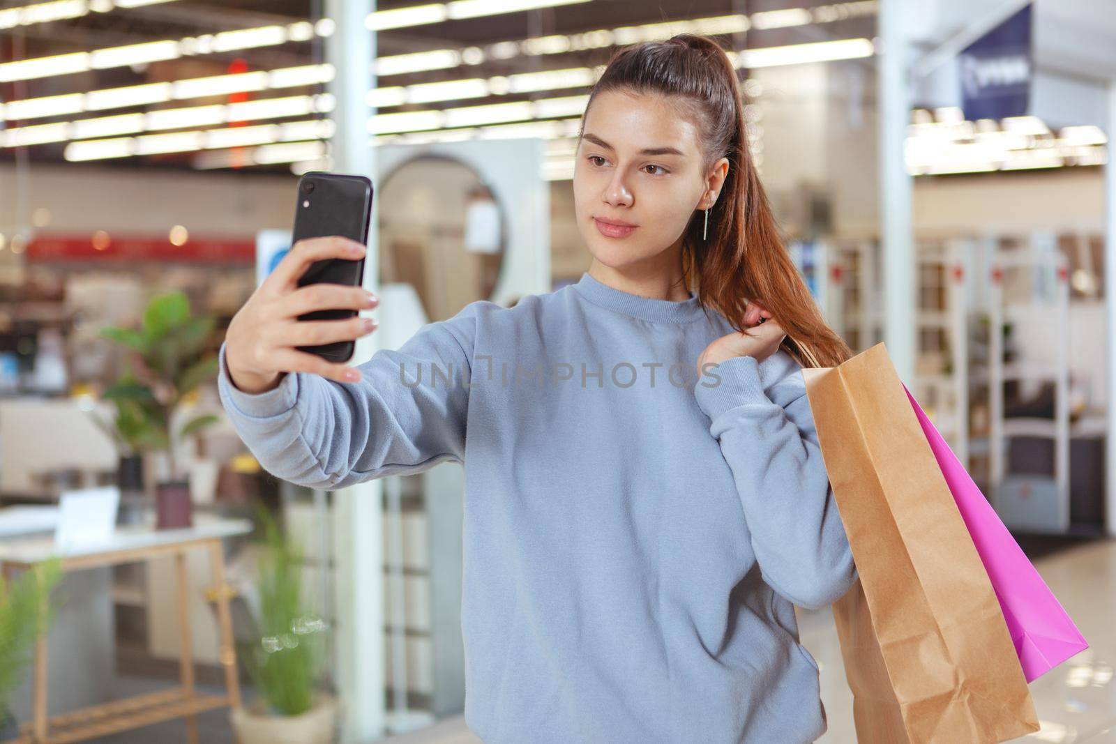 Beautiful young woman taking a selfie with her smart phone while shopping at the mall
