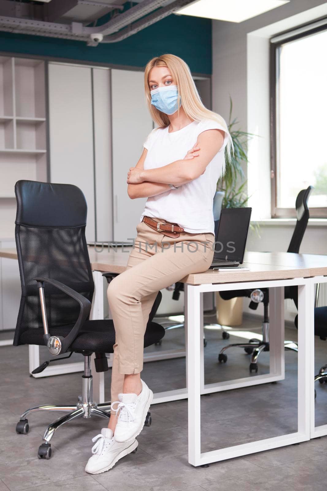 Full length vertical shot of a successful female entrepreneur at her office, wearing medical face mask