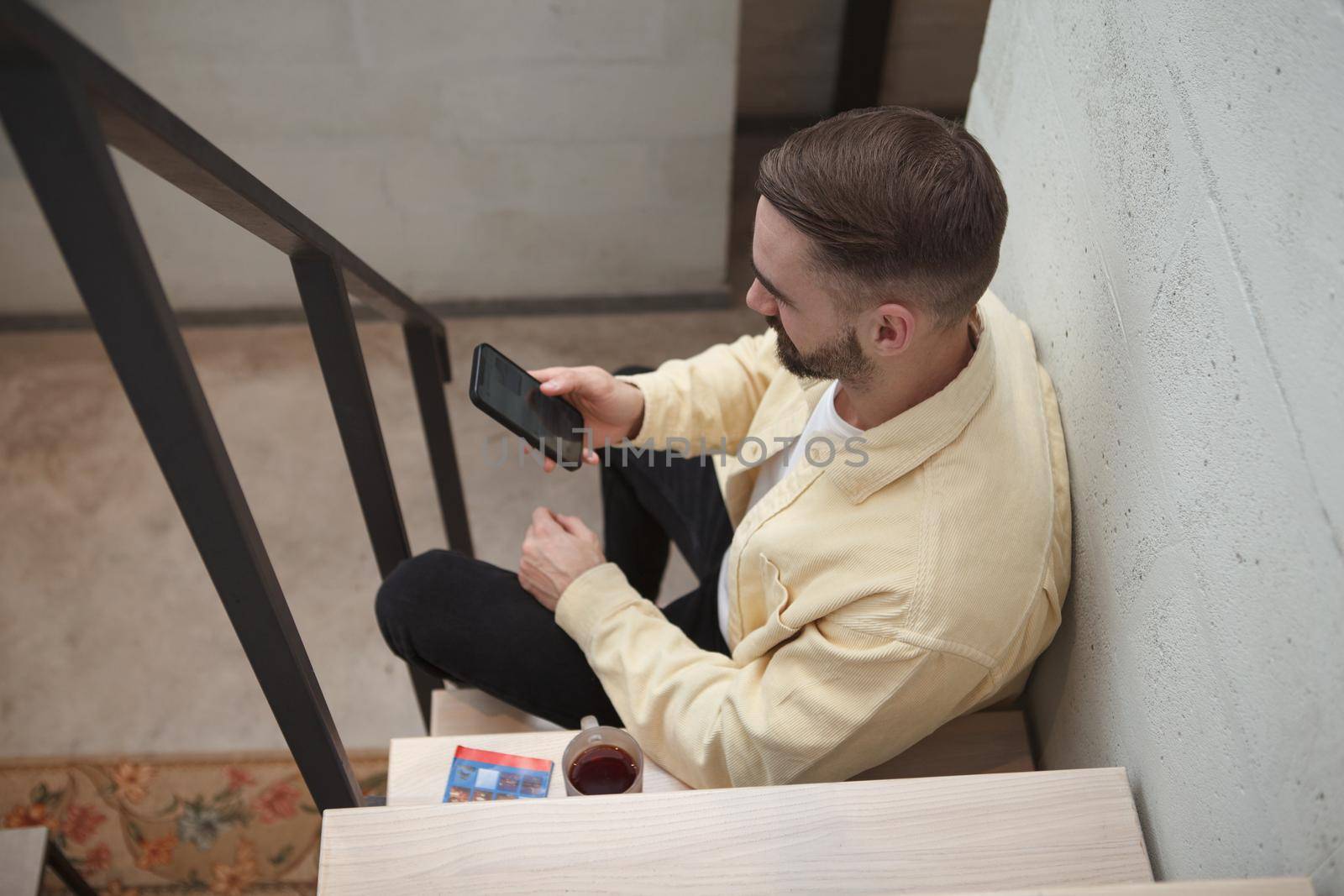 Top view shot of a man texting on his smart phone, sitting on the staircase at the apartment