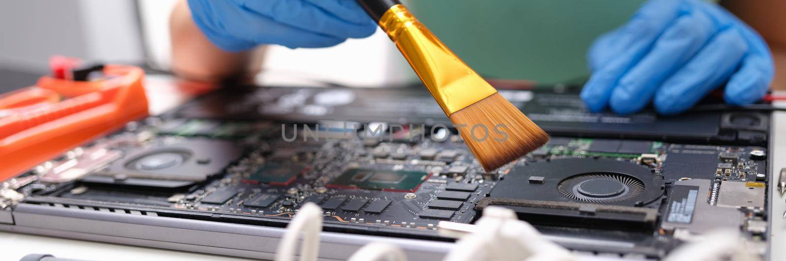 Hands brush the laptop parts from dust, close-up. Repair and maintenance of electronic devices, worker technical engineer