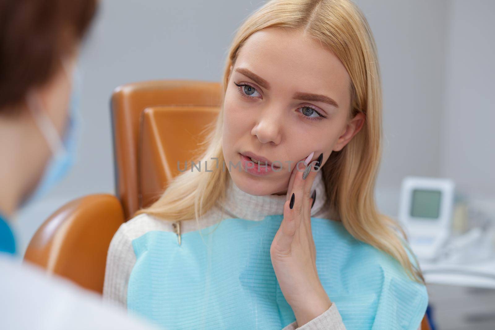 Beautiful young woman suffering from toothache, visiting dentist. Professional dentist preparing for dental examination of her female client with painful cavities. Medicine, health, treatment concept