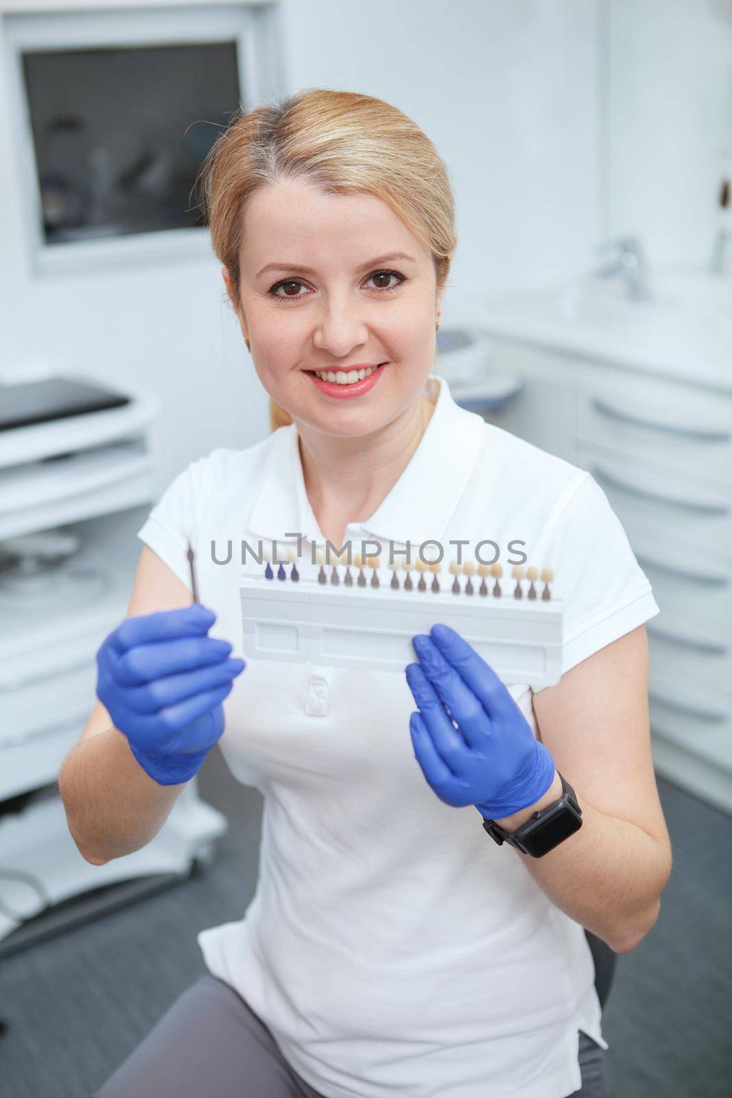 Vertical shot of a cheerful female dentist holding teeth whitening shade guide