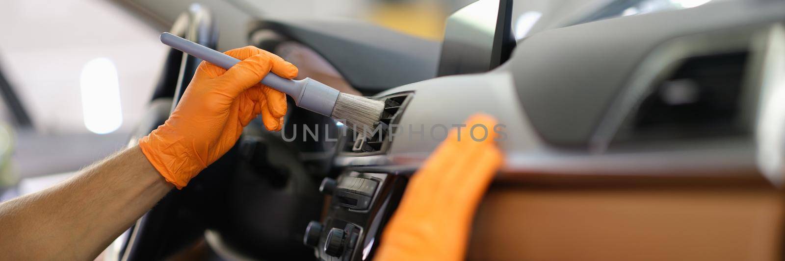 A man brushes the dust inside the car, hands in gloves close-up. Car interior, equipment cleaning service in the automobile