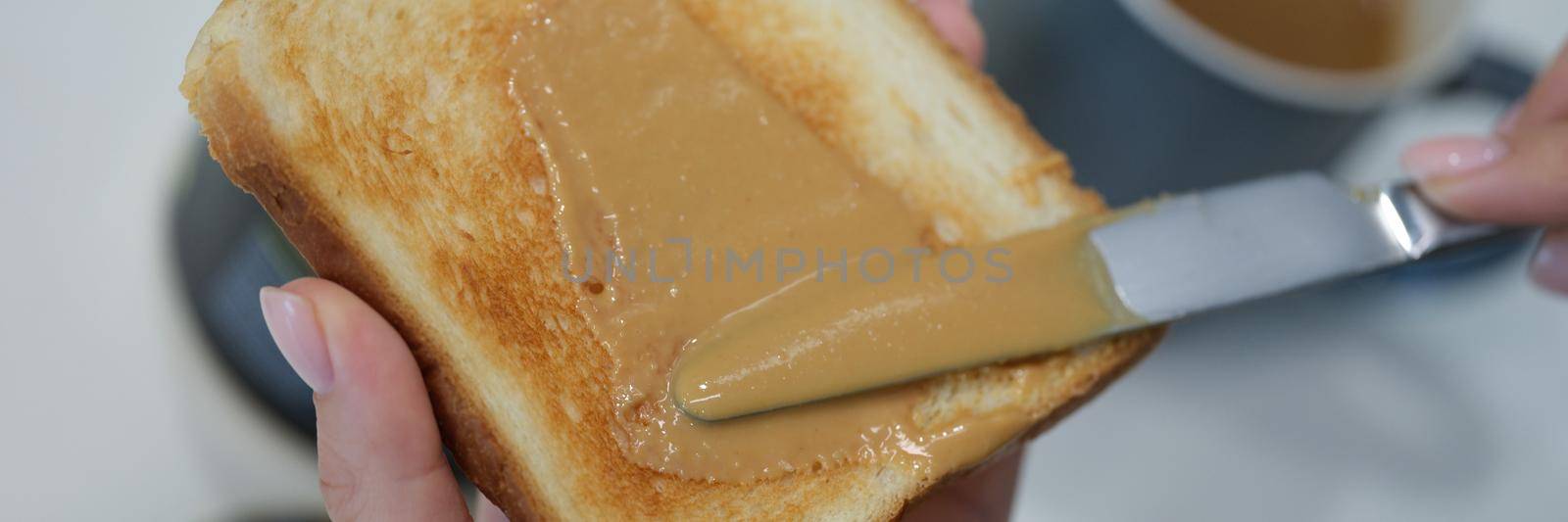 A woman is brushing peanut butter on a toast with a knife, close-up. Chocolate sauce on bread, homemade breakfast