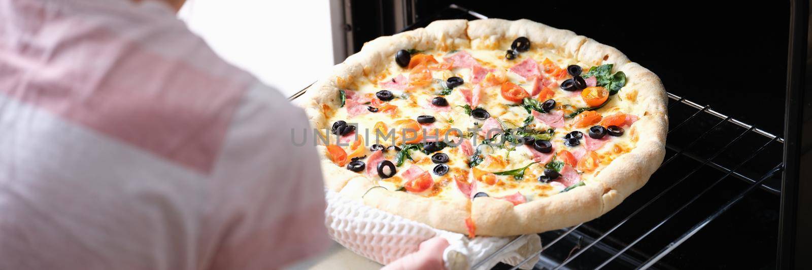 Woman in the kitchen bakes pizza in the oven by kuprevich