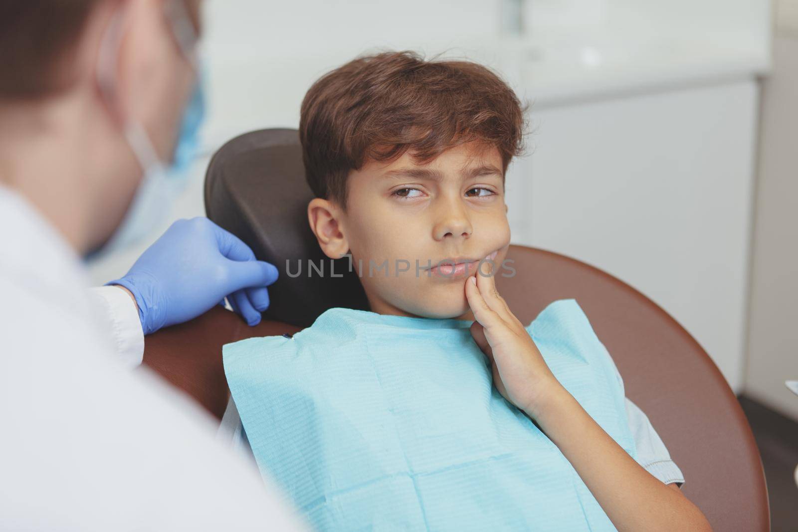 Young boy having toothache, sitting in a dental chair during dental examination. Cropped shot of a professional dentist preparing to cure teeth of a young boy