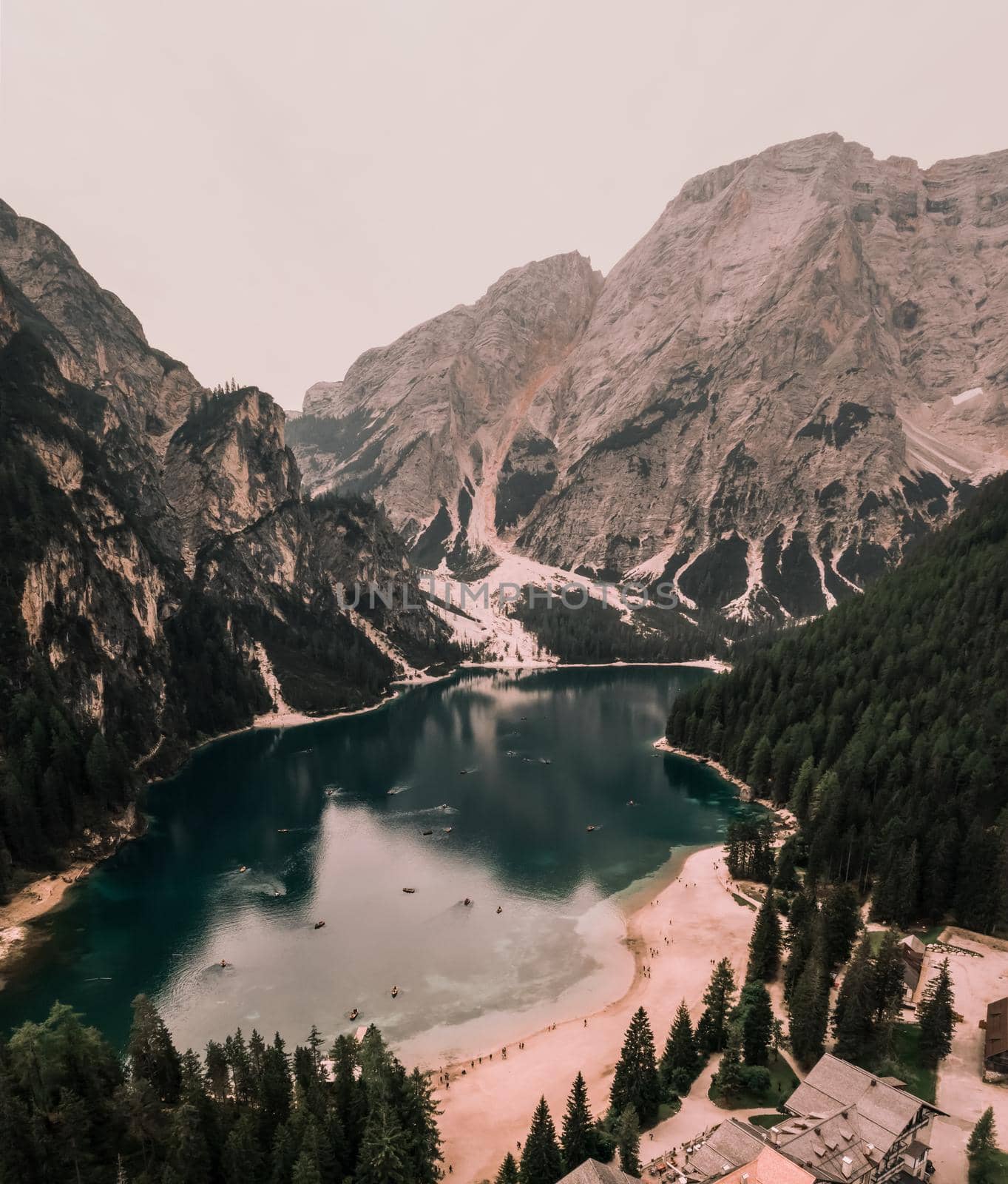 A large clear azure aquamarine green lake with brown wooden boats. High snow-capped stone mountains. Aerial top view from drone.