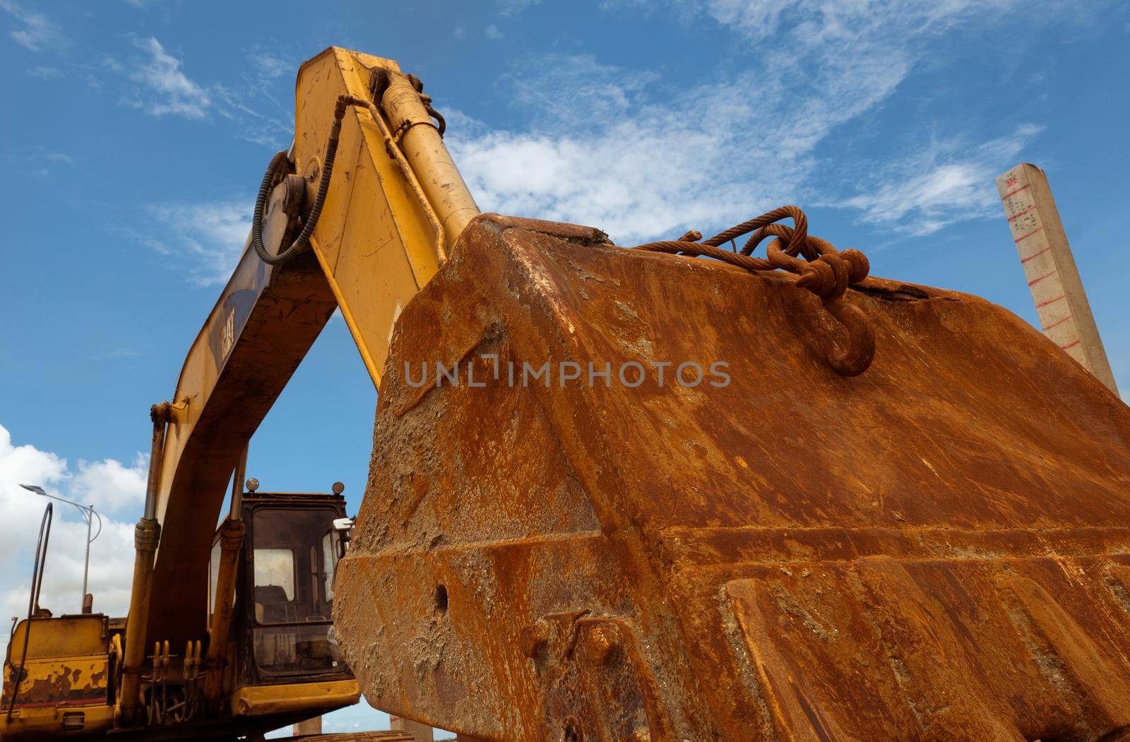 Closeup rusty metal bucket of old backhoe parked at construction site against blue sky. Excavating machine. Earth moving machine. Excavation vehicle. Dirt bucket of old digger. Construction industry.