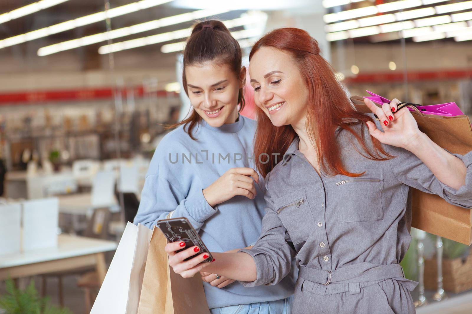 Beautiful women browsing online on smart phone, while walking at the mall with shopping bags