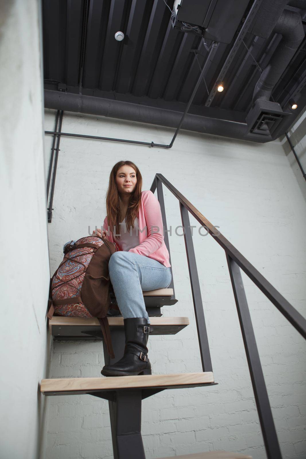 Vertical low angle shot of a beautiful female tourist with a backpack sitting on top of staircase at the hotel room