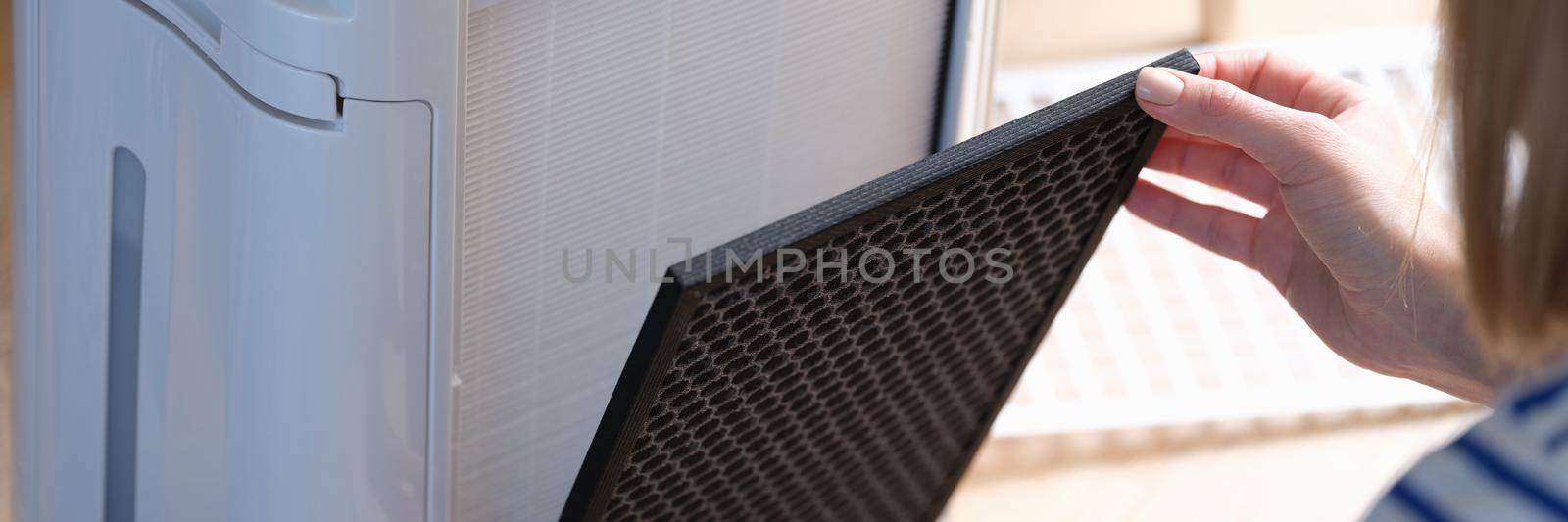 A woman removes a filter from an air-purifying system, close-up. Dust collector replacement and cleaning, household appliances