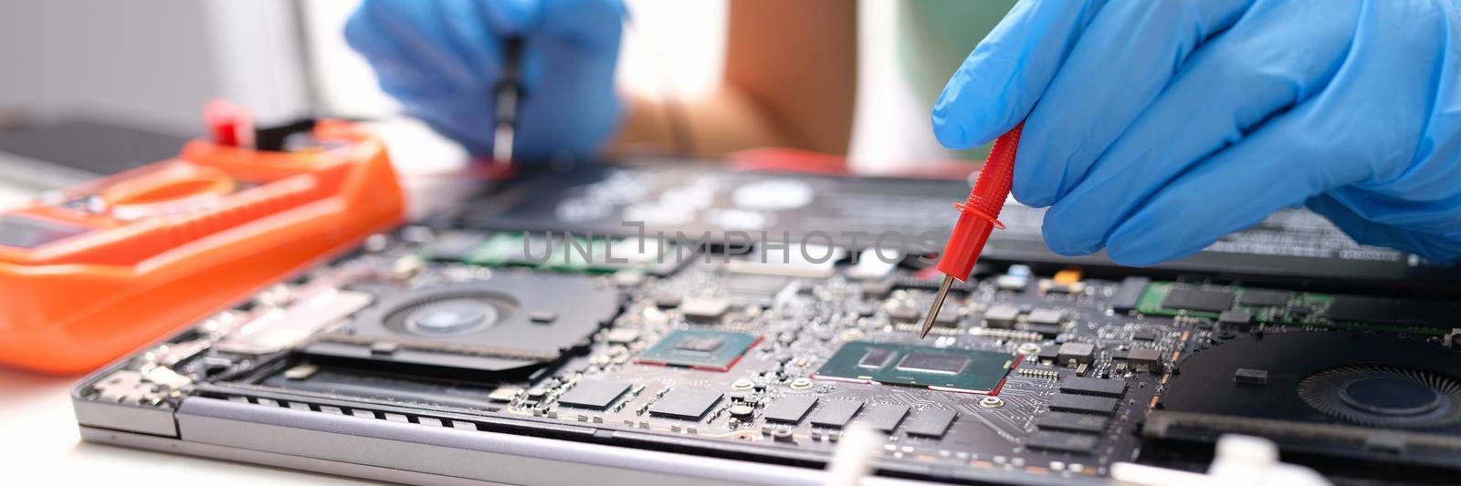 Laptop repair, gloved hands holding a voltage meter for electronics. Processor testing, diagnostics motherboard