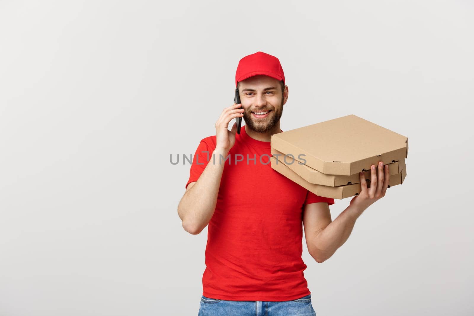 Portrait of a smiling delivery man in red cap talking on mobile phone while holding pizza boxes isolated on the white background.