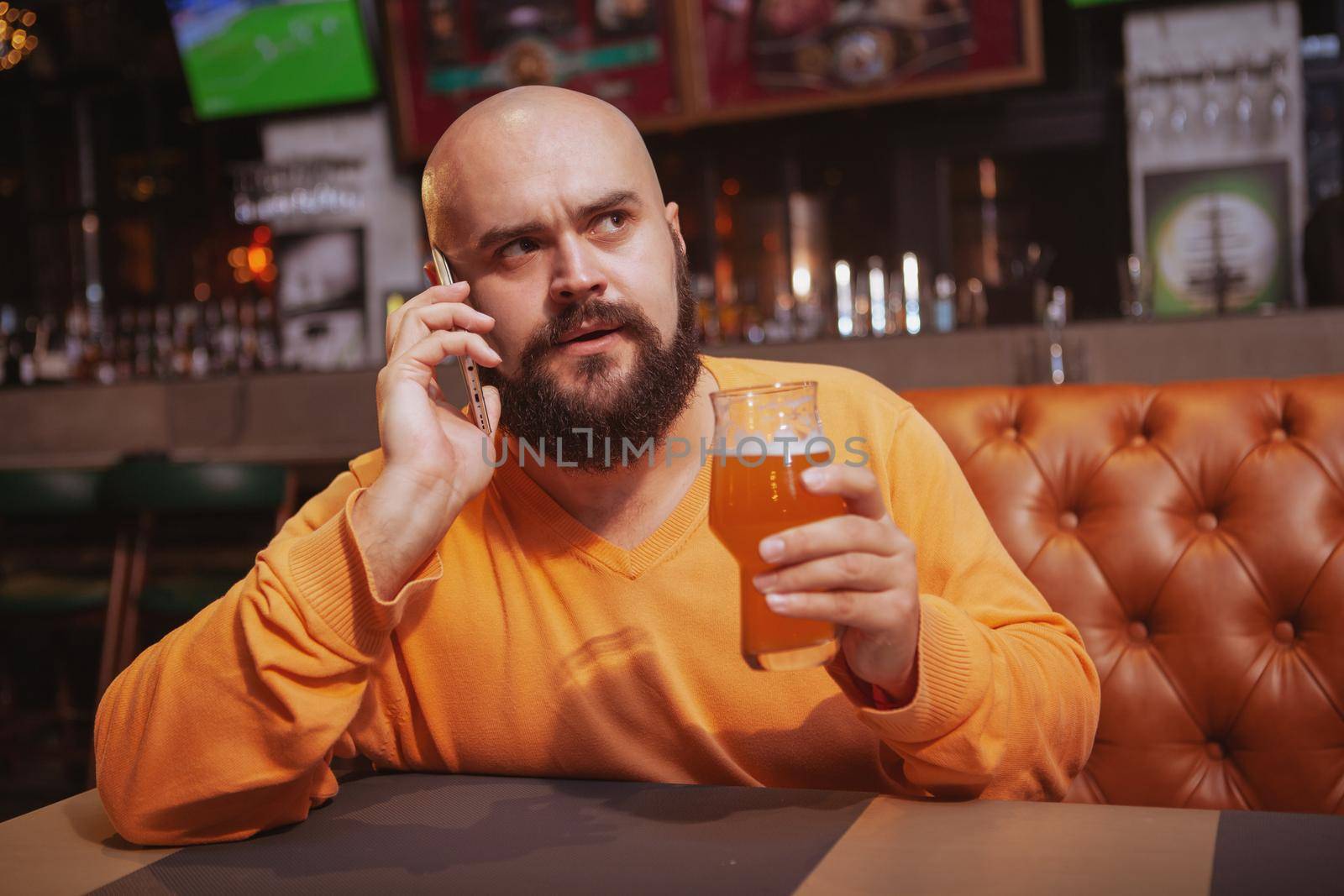 Mature man talking on the phone while drinking beer at the pub