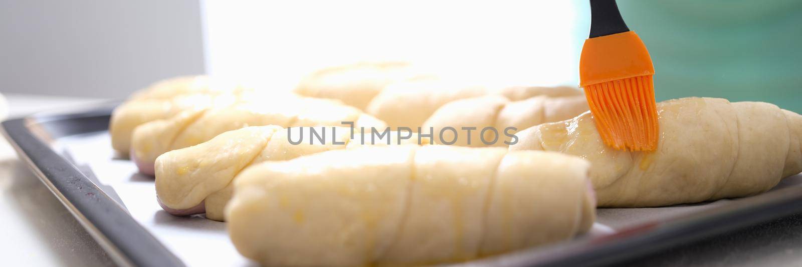 A woman is brushing dough products with a brush, close-up. Bakery making sausages in dough, cooking, fast food