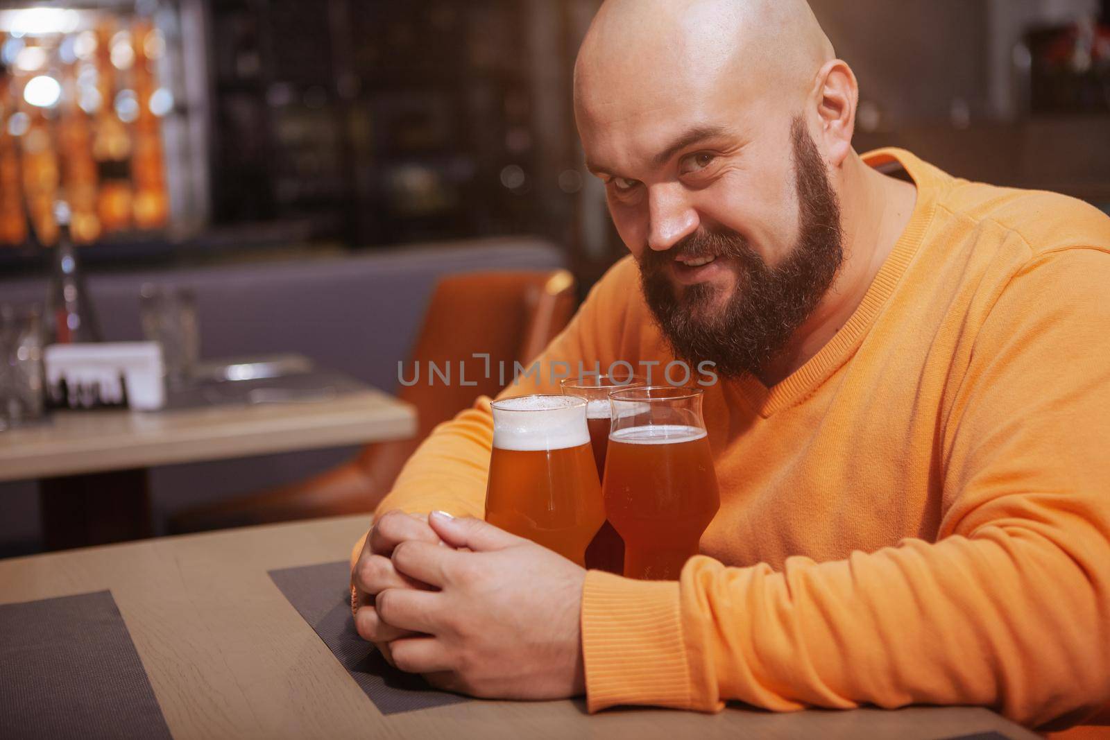 Bearded man smiling devilishly to the camera embracing three beer glasses, copy space
