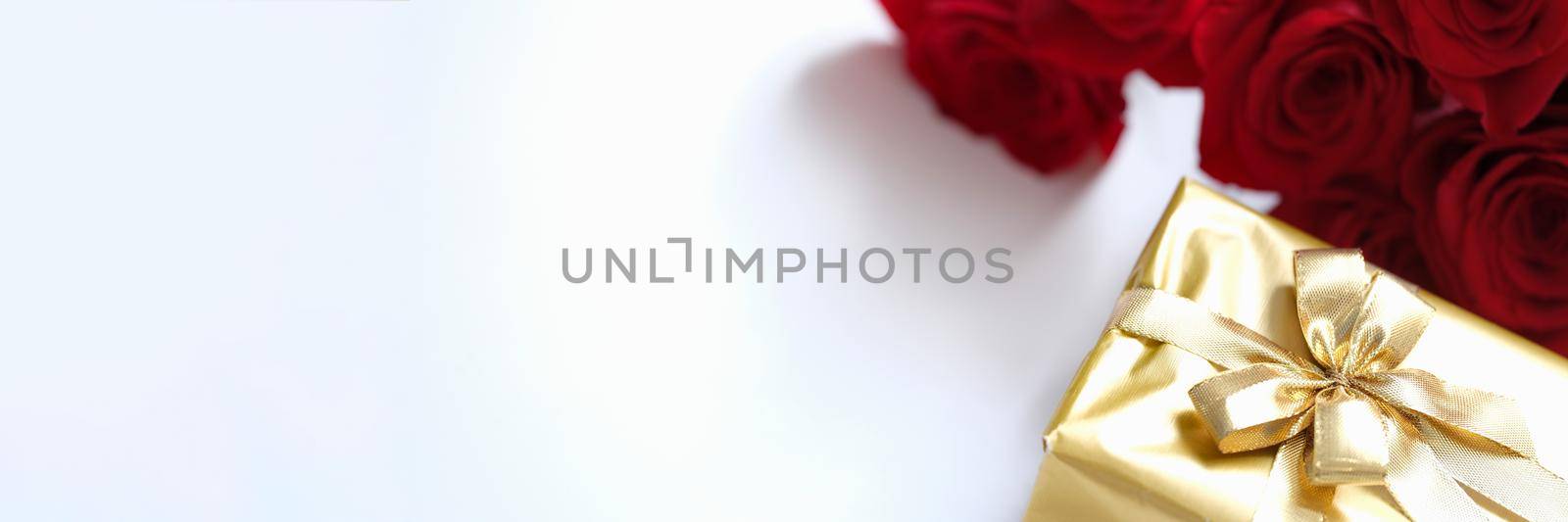 Beautifully wrapped gift in gold paper with ribbon, mocap. Red roses and gift wrap on a white background. Holiday