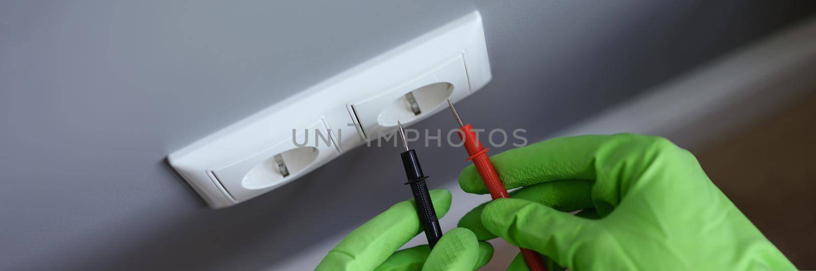 Hands in gloves measure the voltage in the socket with a tool, close-up. Repair of electrical wiring in the apartment