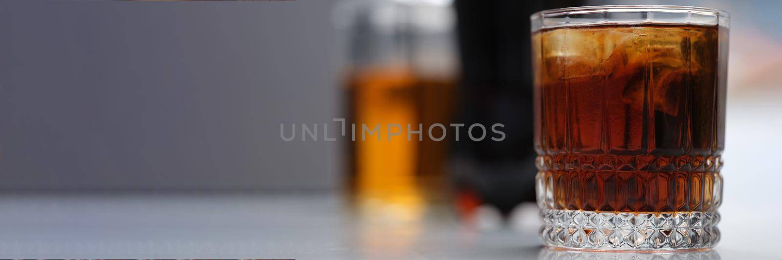 Full glass of alcoholic drink with ice on the table, close-up. Alcohol addiction, alcohol overdose, drunkenness