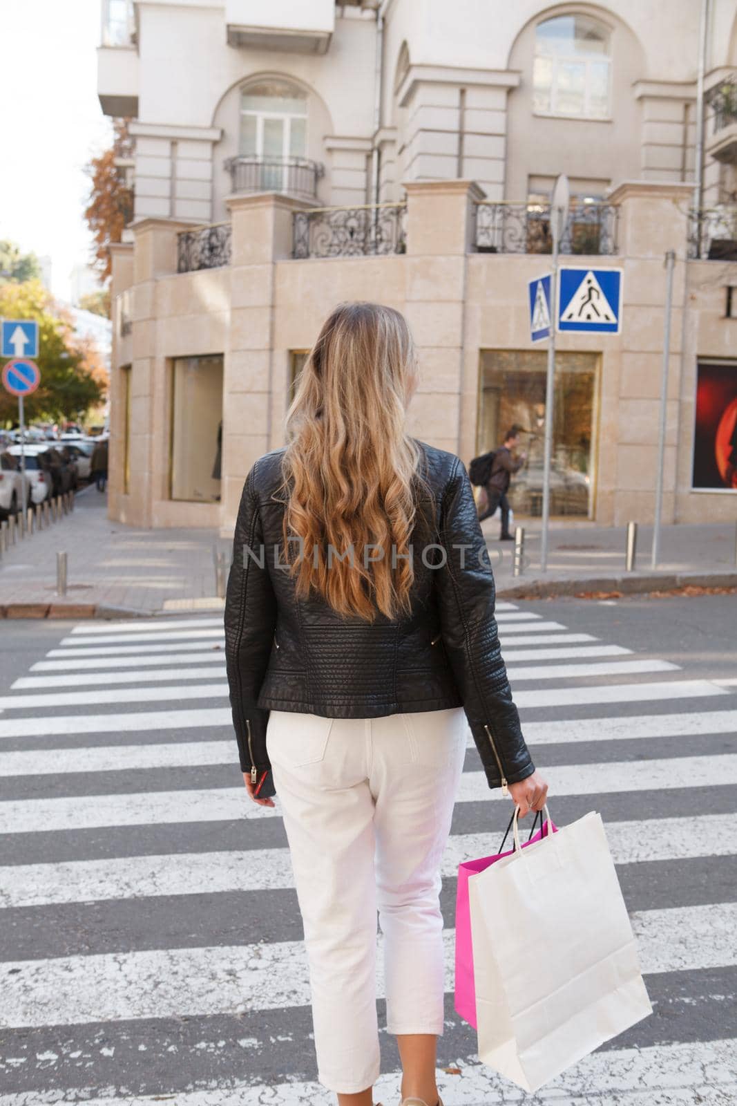 Vertical cropped rear view shot of a woman walking with shopping bags in the city on crosswalk
