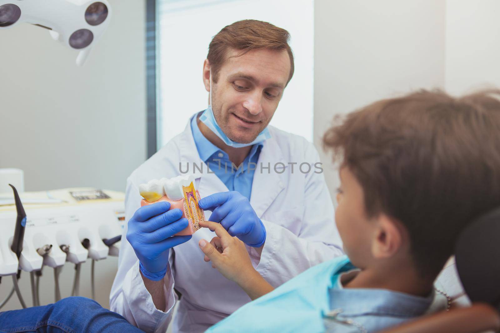 Experienced friendly dentist working at his clinic, talking to the patient, showing tooth model.Cheerful male dentist educating child about dental hygiene
