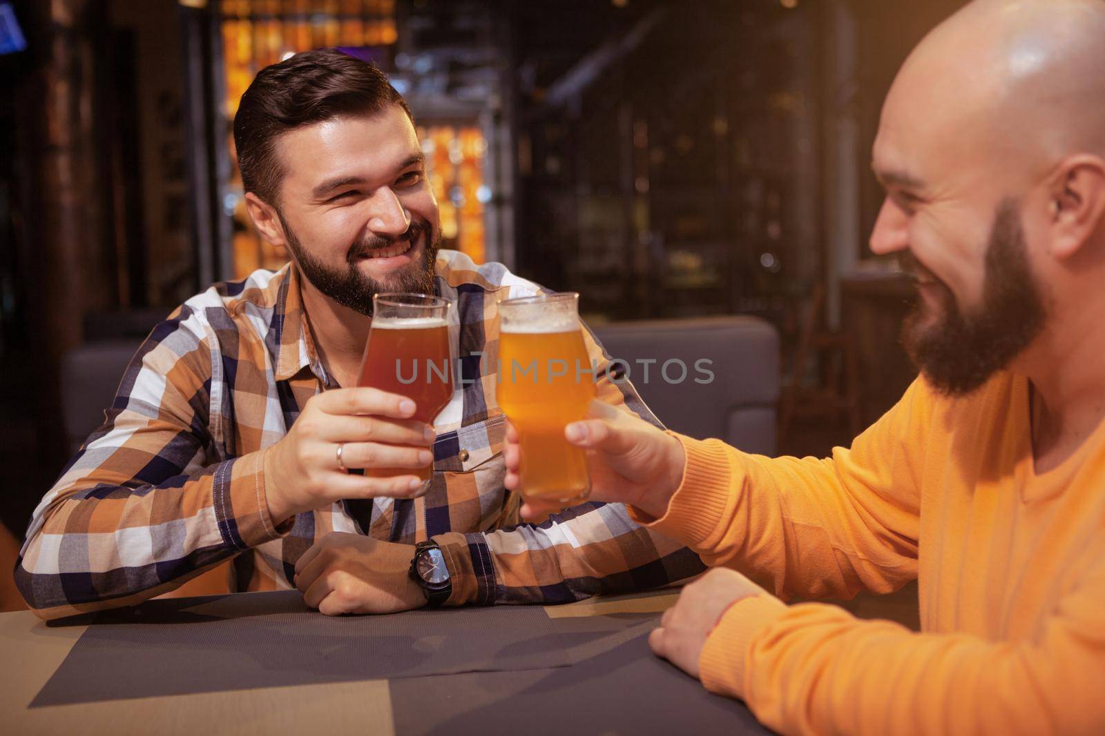 Cheerful male friends clinking their beer glasses, celebrating at the pub